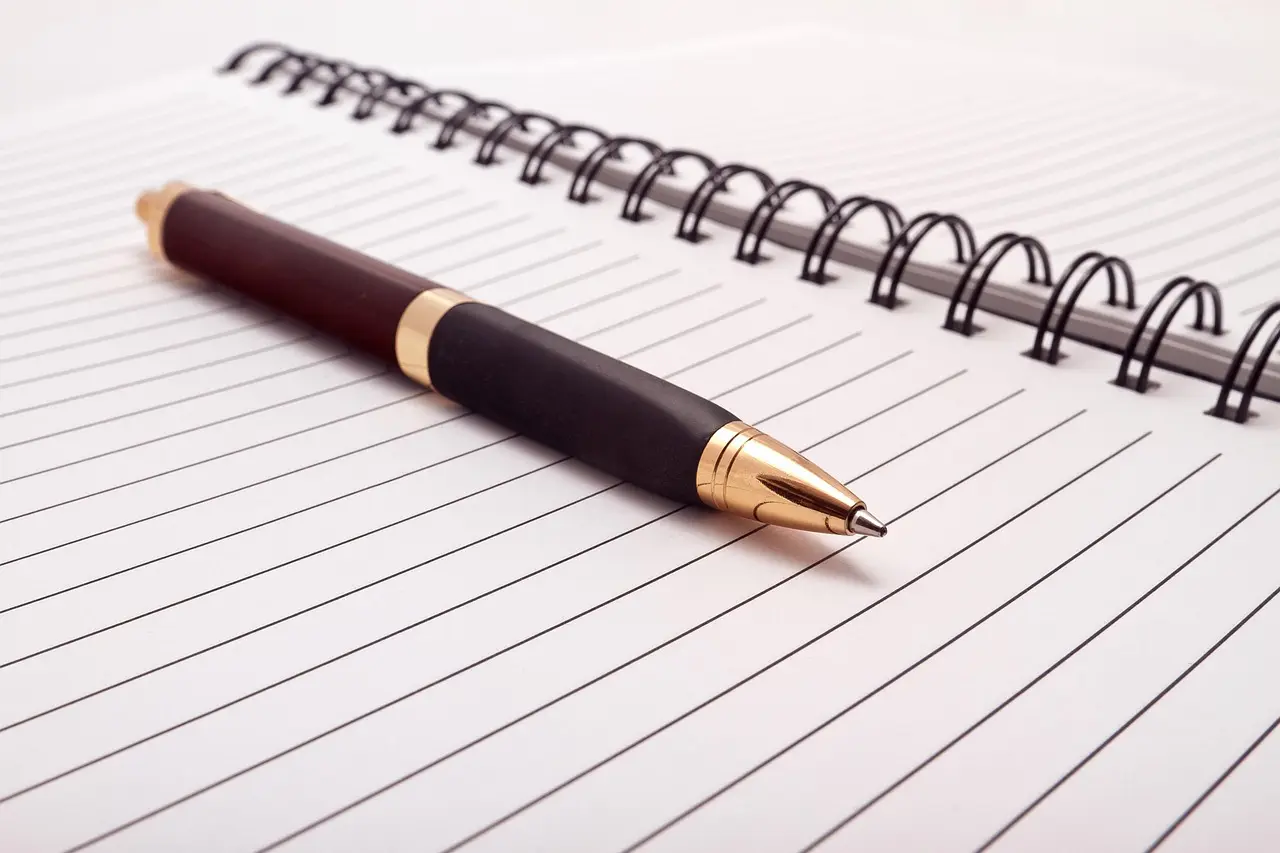 An open blank notebook with a pen beside it on a desk